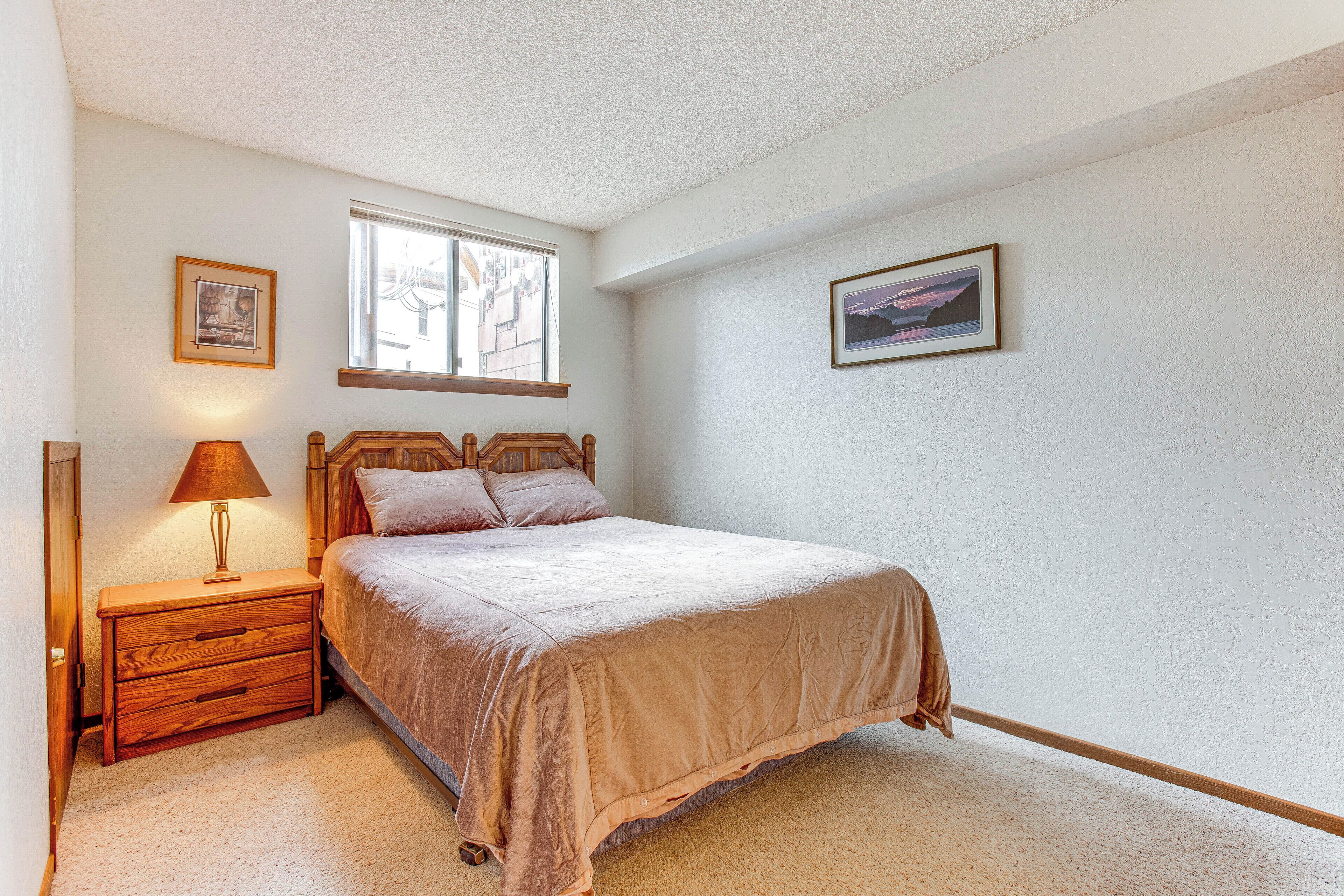A bedroom with a bed, nightstand, lamp, window, and two framed pictures on the wall.