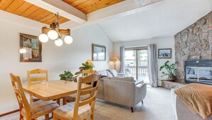 Ein gemütliches Wohnzimmer mit einem Holzesstisch, Stühlen, einem grauen Sofa und einem Steinkamin.