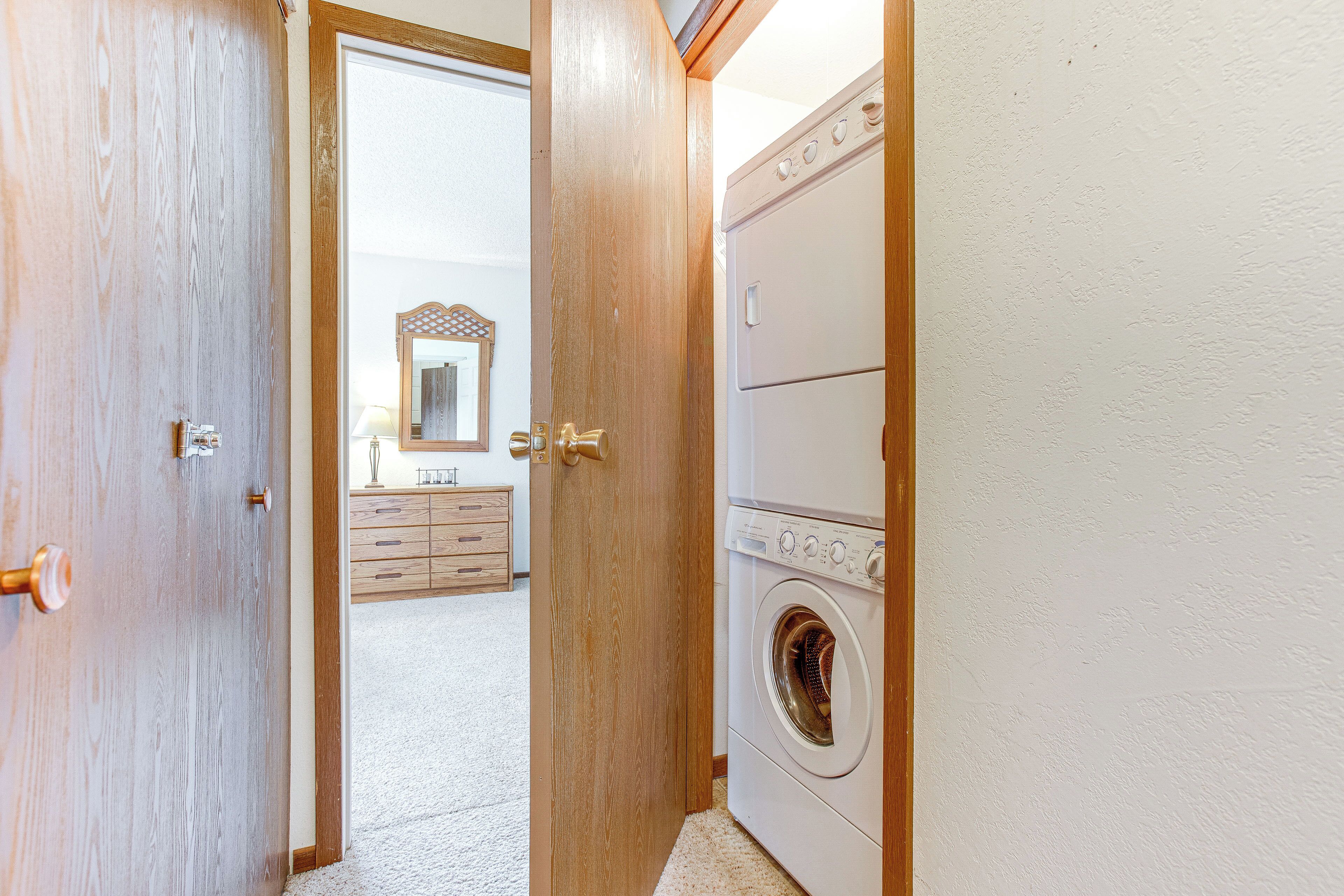 A laundry room with a washing machine and dryer, wooden doors, and a dresser with a mirror in the background.