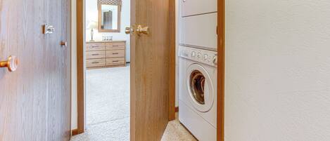 A laundry room with a washing machine and dryer, wooden doors, and a dresser with a mirror in the background.