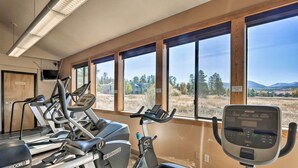 Ein Fitnessraum mit mehreren Trainingsgeräten, großen Fenstern und Blick auf eine Landschaft, sowie eine Tür mit der Aufschrift 'Exercise Room'.