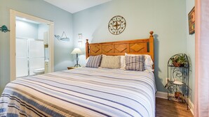 A bedroom with a large bed, a wooden headboard, a bedside table with a lamp, and a wall-mounted decorative item.