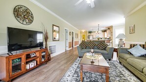 A living room with a flat-screen TV, wooden entertainment center, patterned rug, and a sofa with decorative pillows.