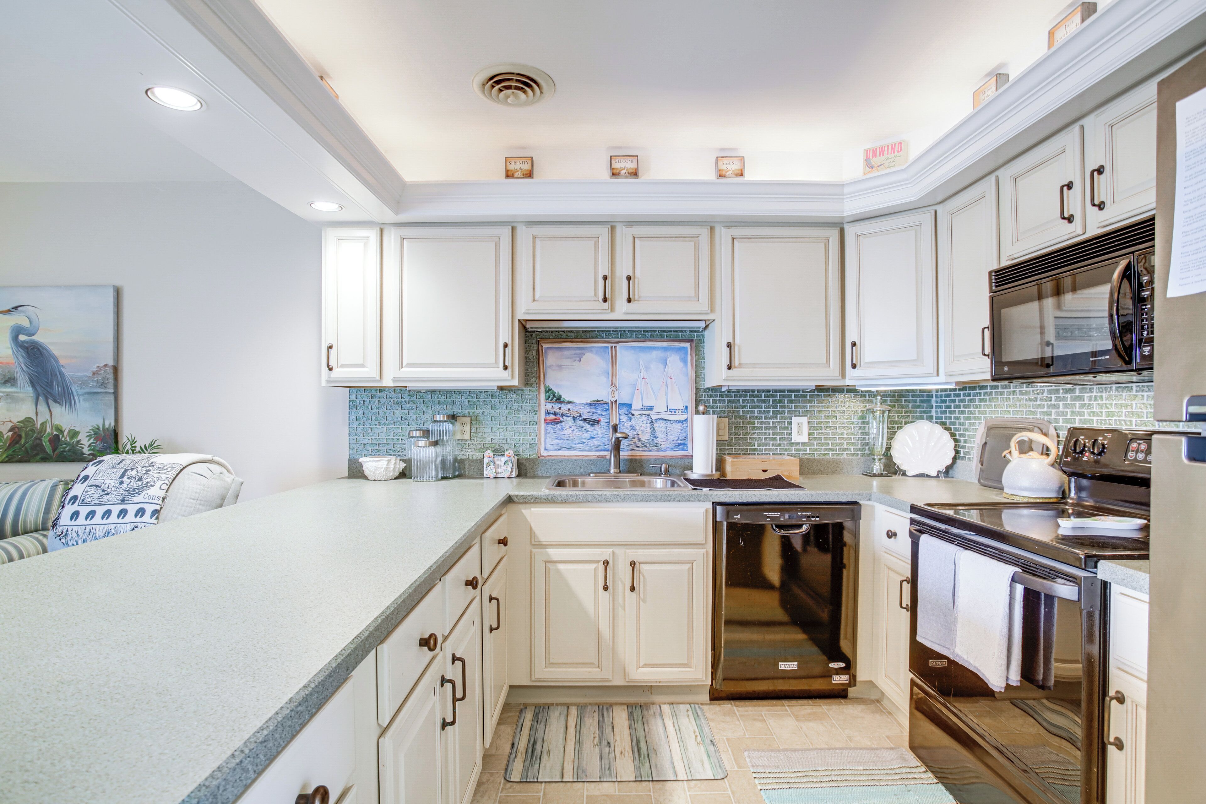 A modern kitchen with white cabinetry, a large island, stainless steel appliances, and a tiled backsplash.
