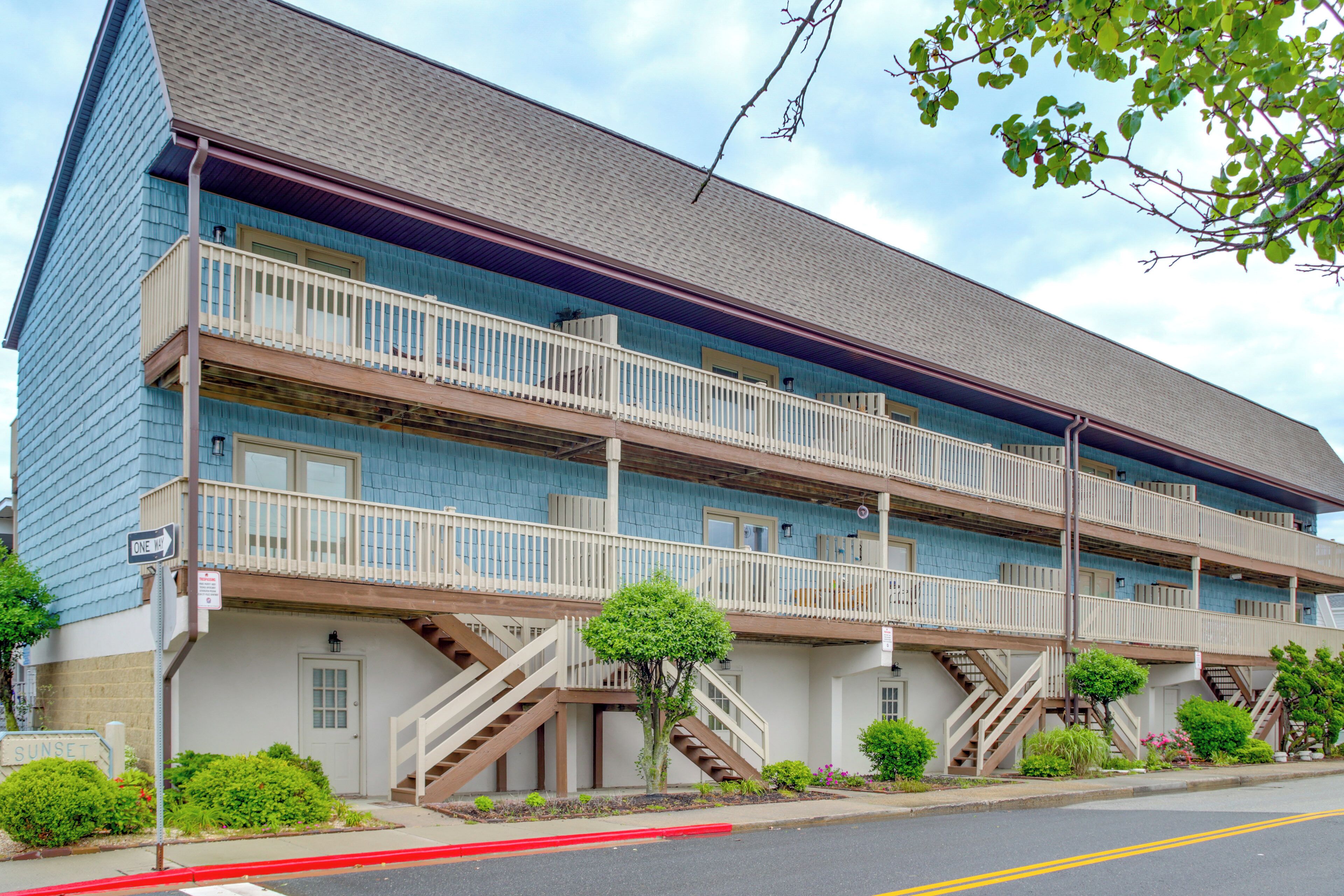 A multi-story building with a balcony on each floor, a staircase on the ground level, and a sign that reads "SUNSET".