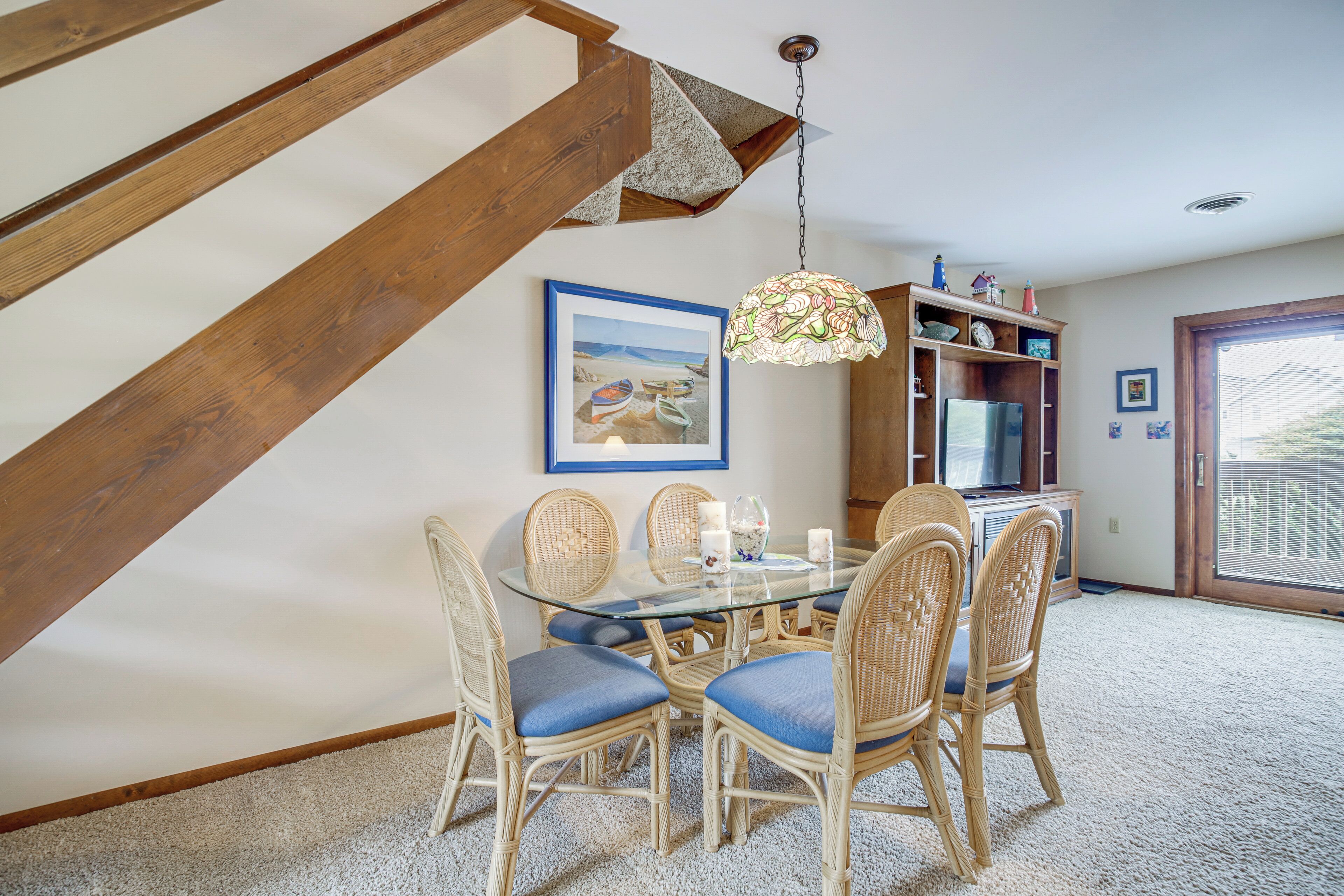 A dining area with a glass table, wicker chairs, and a hanging light fixture.