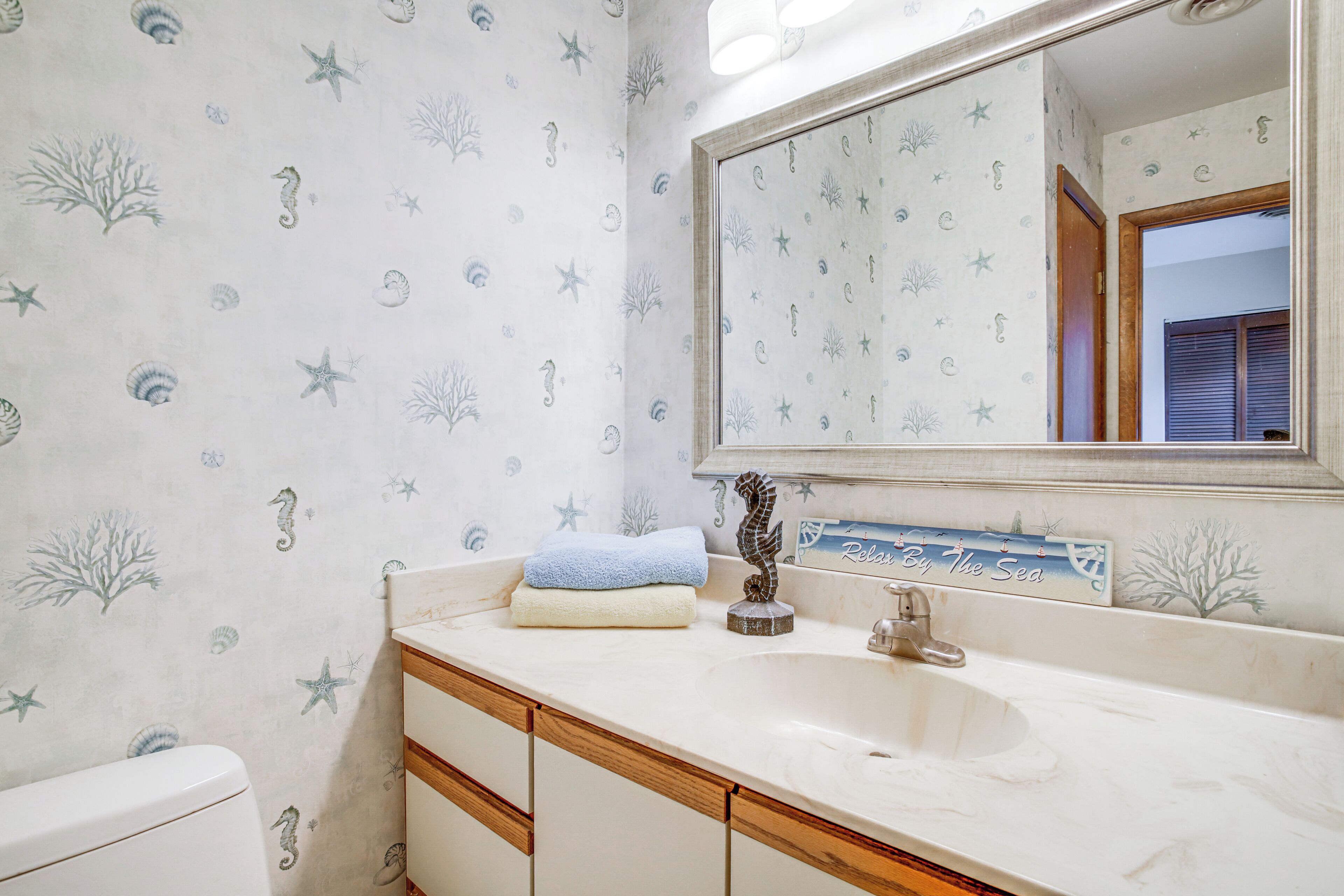 A bathroom with a sea-themed wallpaper, a sink, and a mirror.