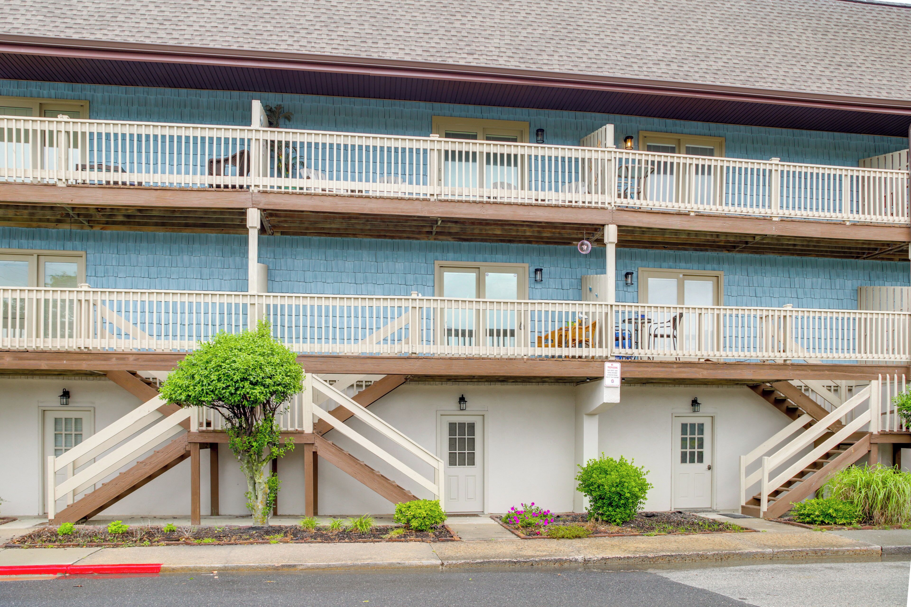 A multi-story building with balconies, a staircase, and a small tree in the front yard.