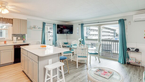 A modern kitchen with a central island, dining area with chairs, and a balcony with a view.