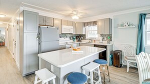 A modern kitchen with a central island, bar stools, and a ceiling fan.