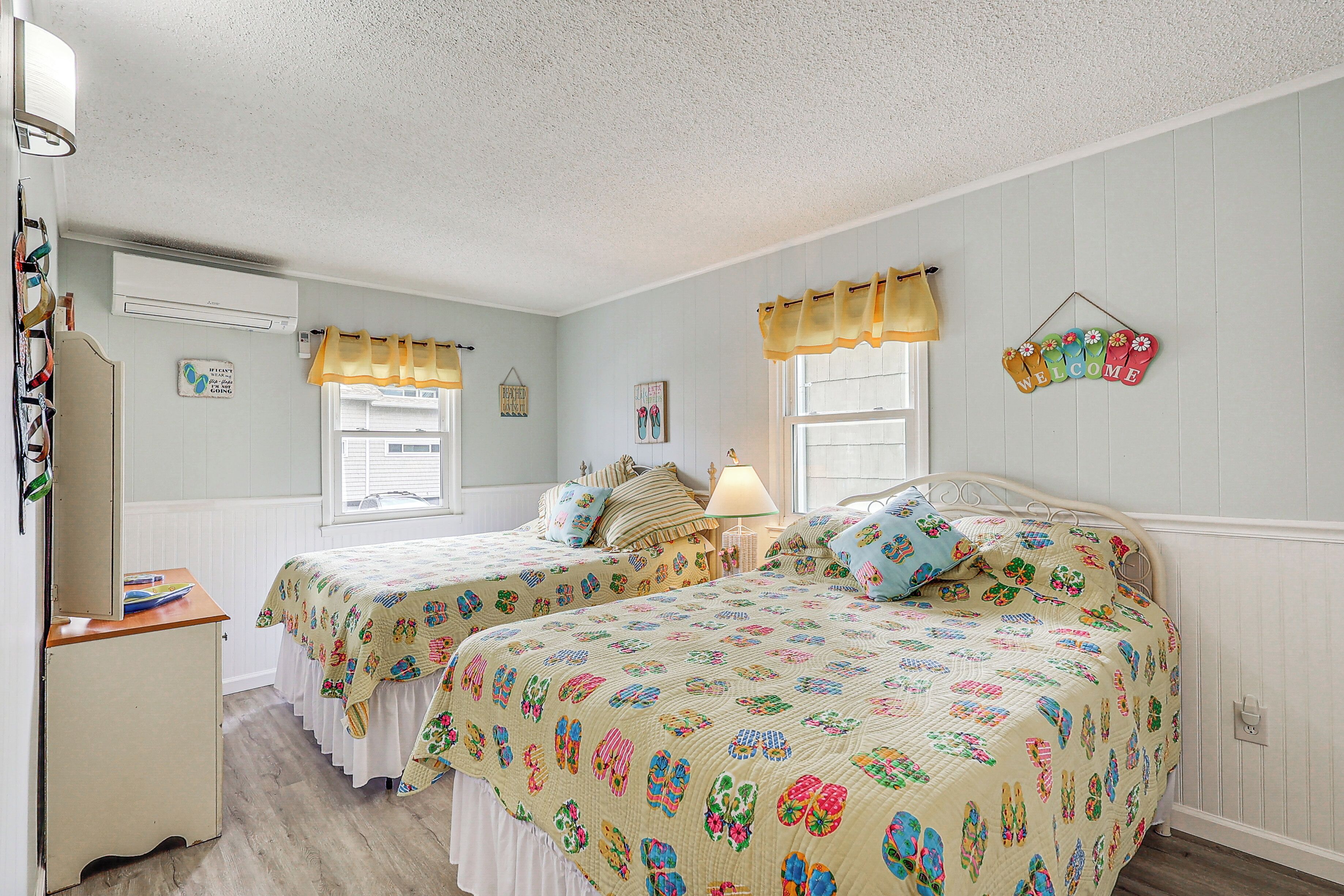 A bedroom with two beds, a dresser, and a window with curtains.