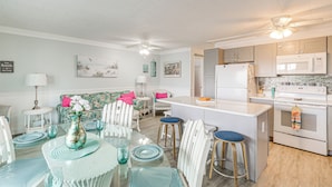 A modern kitchen with white appliances, a dining area with a glass table, and a ceiling fan.