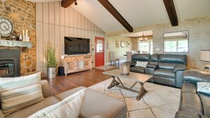 Ein geräumiges Wohnzimmer mit Steinwand, Holzbalken, Kamin, Fernseher, Ledersofas und einem Couchtisch.