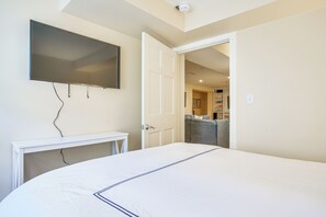 A bedroom with a large bed, a TV mounted on the wall, and a door leading to a hallway. - Stunning Ocean View! Beachfront Nantucket Retreat (Nantucket)