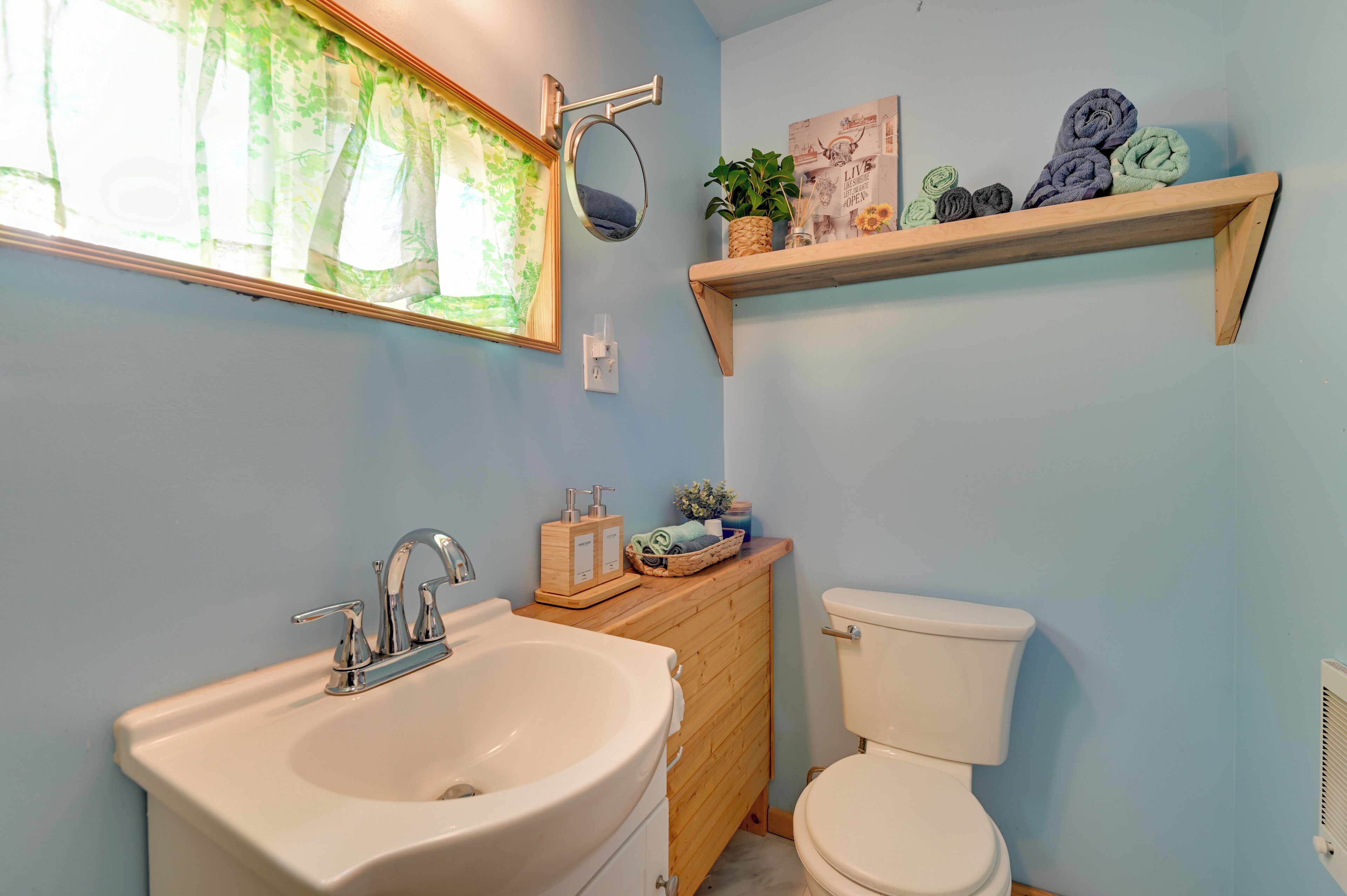 A bathroom with a sink, mirror, toilet, and a shelf with towels.