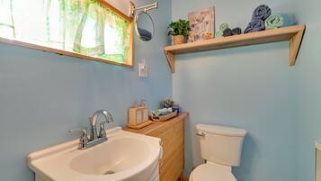 A bathroom with a sink, mirror, toilet, and a shelf with towels.