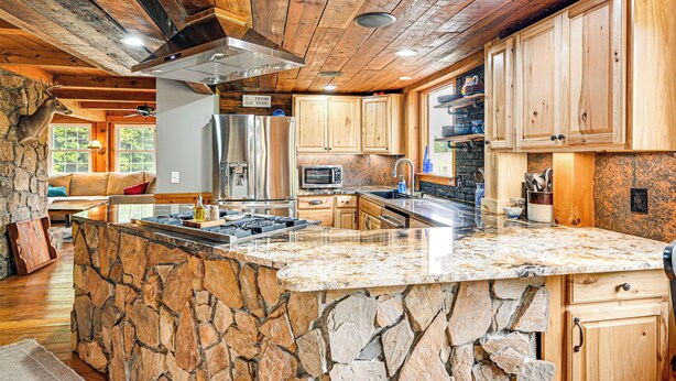 Una cocina rústica con una isla de piedra, armarios de madera y una pared de piedra.
