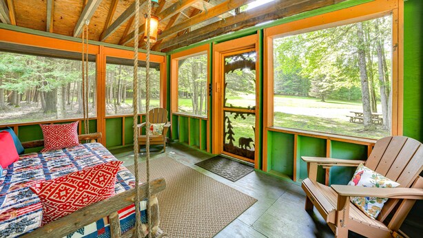 A cabin with a bed, a chair, and a view of the forest. - Cardinal Pines Cabin on 8 Acres - Dog Friendly! (New Berlin)