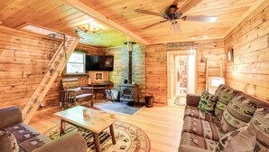 A cozy cabin interior with a wooden floor, a sofa, a table, a fireplace, and a television. - Cardinal Pines Cabin on 8 Acres - Dog Friendly! (New Berlin)