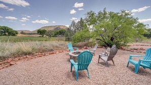 An outdoor seating area with four Adirondack chairs around a fire pit, set on a gravel surface with a view of a hilly landscape and trees under a clear sky. - Red Rock State Park Views: Sedona Home w/ Fire Pit (Sedona)