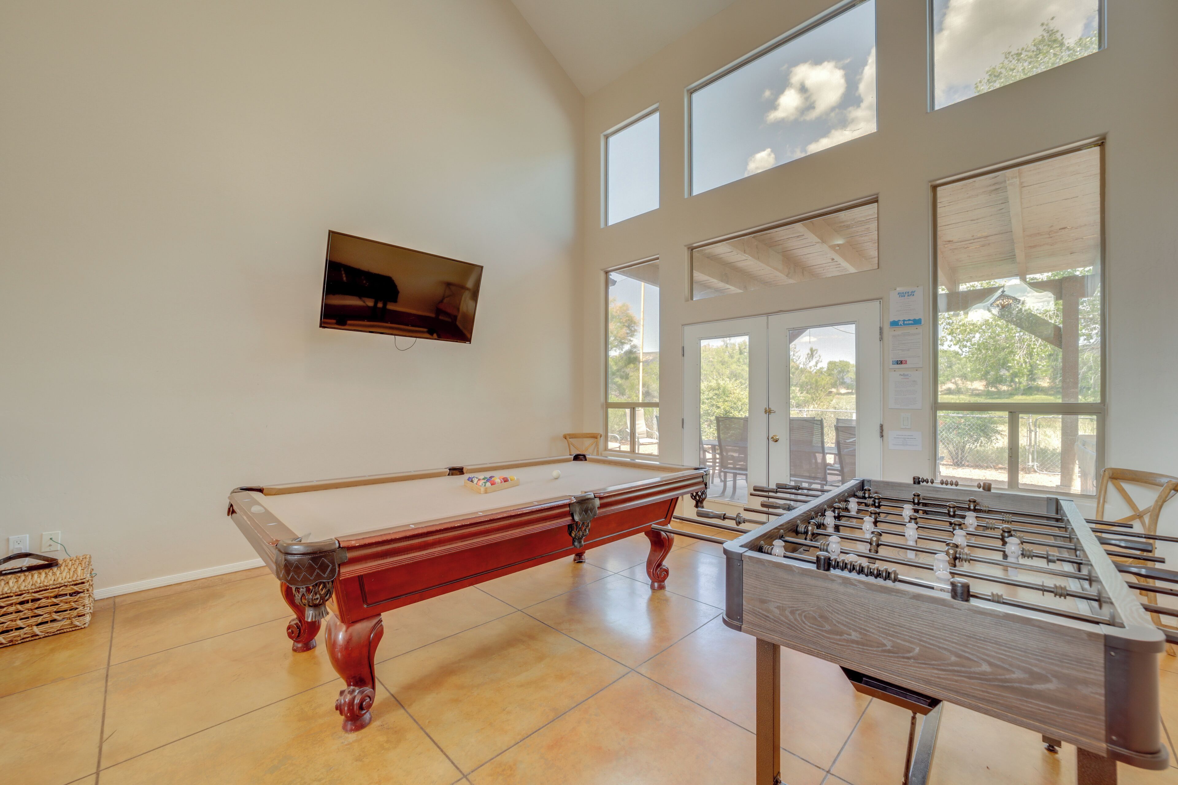 A spacious room with a pool table, foosball table, and large windows offering natural light.