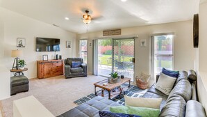 A spacious living room with a leather sofa, a wooden coffee table, and a black leather chair. There is a television mounted on the wall and a ceiling fan.