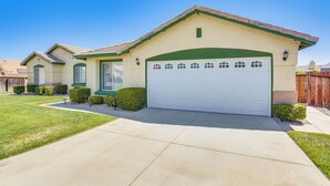 A single-story house with a white garage door, green trim, and a small front yard with a lawn and a few bushes.