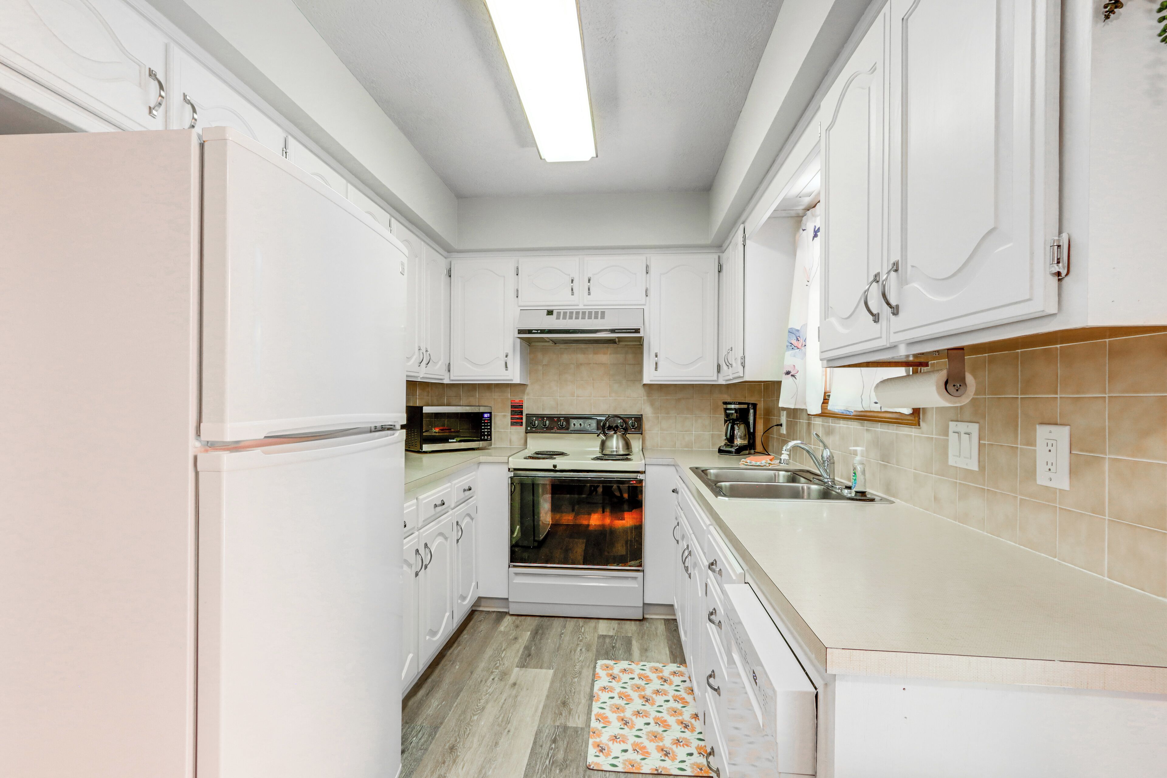 A modern kitchen with white cabinets, a built-in oven, a microwave, and a sink.