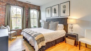 A bedroom with a brick wall, a large window, a bed with a striped blanket, and a bedside table with a lamp. - Near Trail: Dtwn Eagle Ranch Condo w/ Balcony (Eagle)