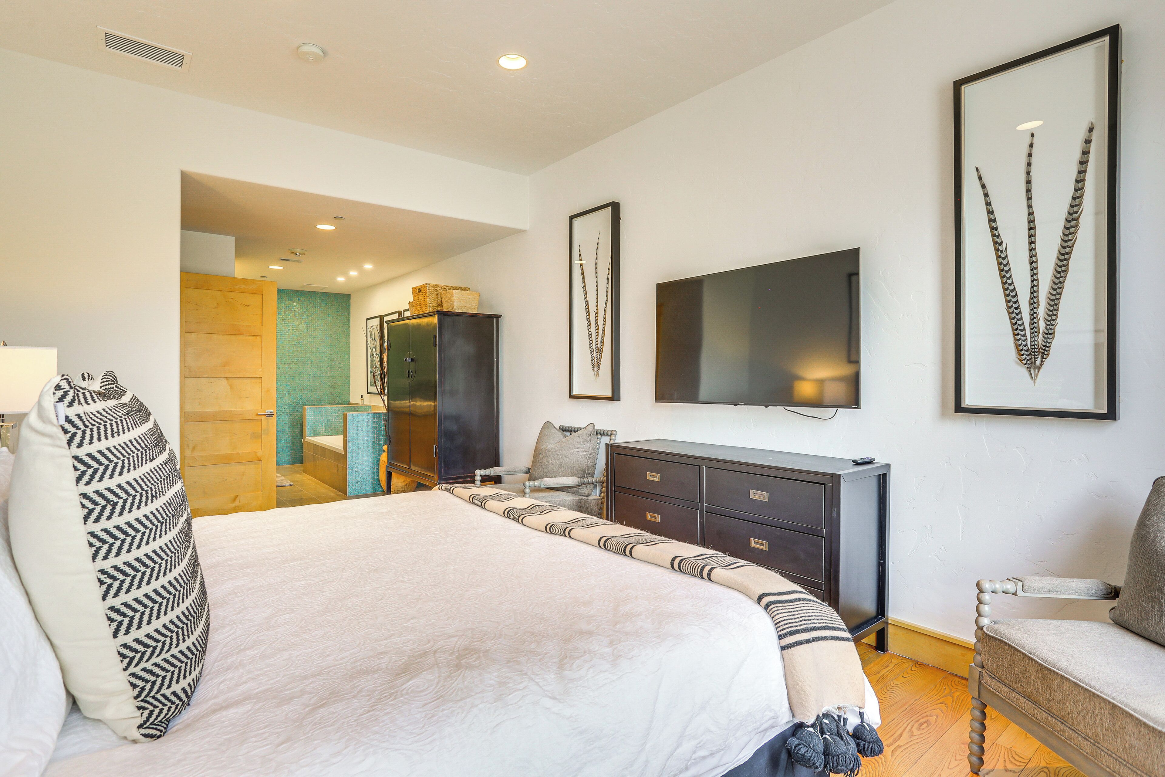 A bedroom with a large bed, a dresser, a chair, and a television on the wall.