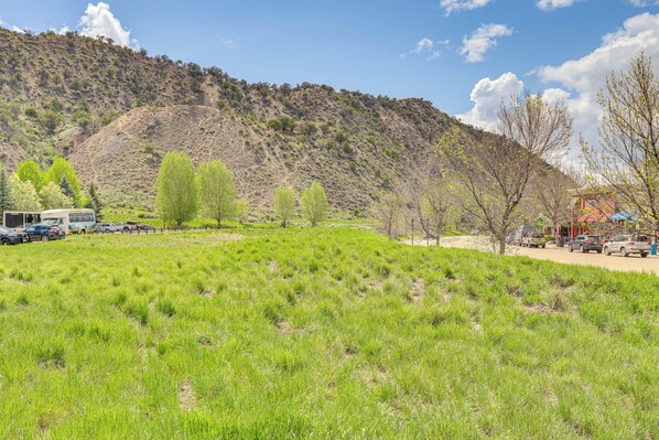 A grassy field with a mountain in the background, a few trees, and parked cars. - Near Trail: Dtwn Eagle Ranch Condo w/ Balcony (Eagle)