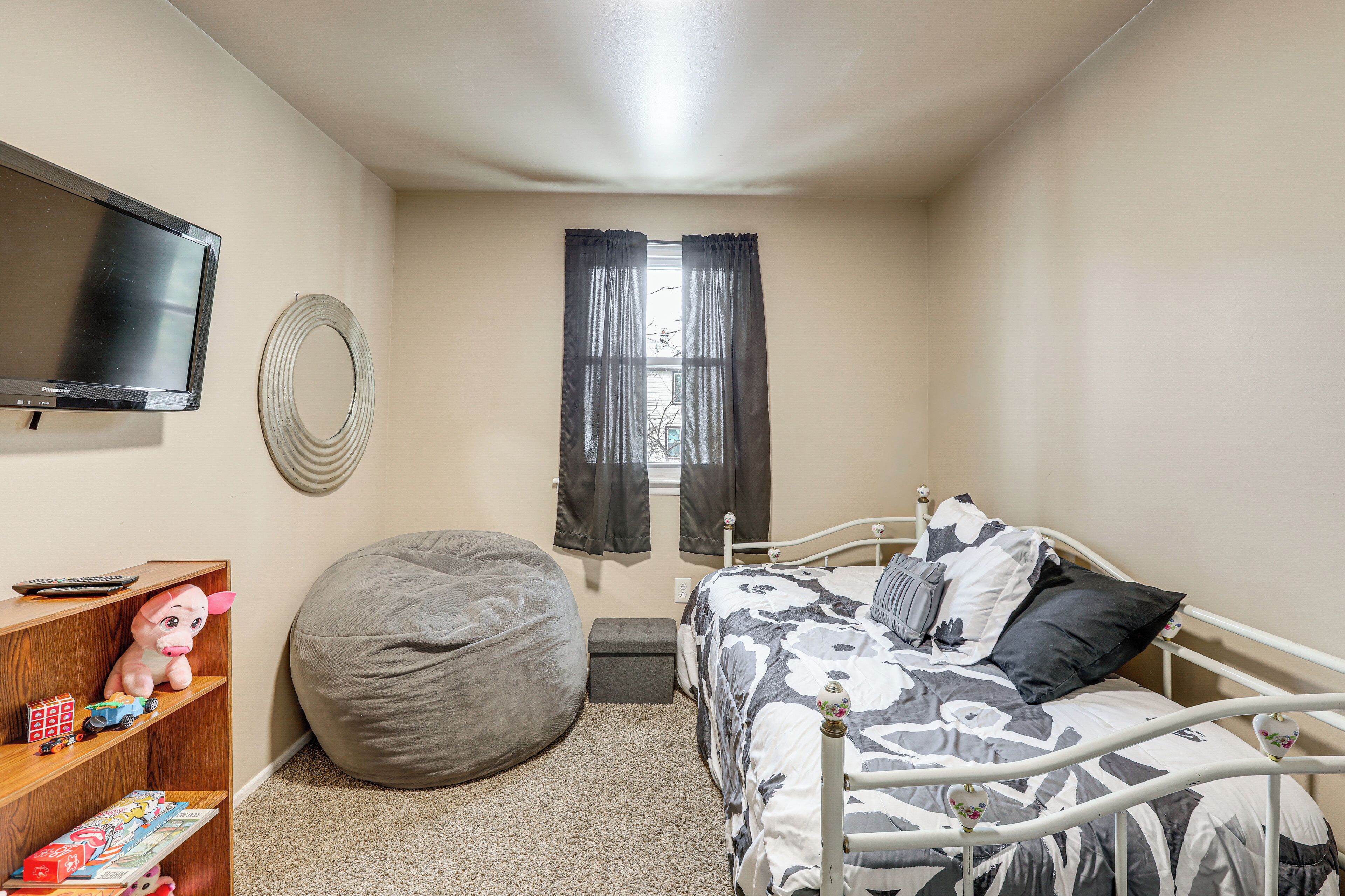 Een slaapkamer met een bed, een relaxfauteuil, een televisie en een plank vol speelgoed.
