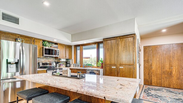 A modern kitchen with a large island, bar stools, stainless steel appliances, and wooden cabinets. - Oro Valley Retreat w/ Pool & Breathtaking Views! (Oro Valley)