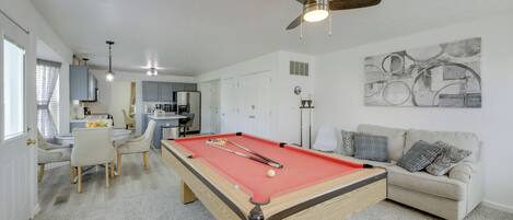 Une table de billard dans un salon, avec un canapé et un tableau accroché au mur.