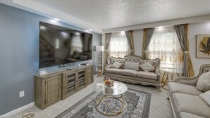 Ein Wohnzimmer mit großem Flachbildfernseher, einer Couch, einem Couchtisch und einem gemusterten Teppich.