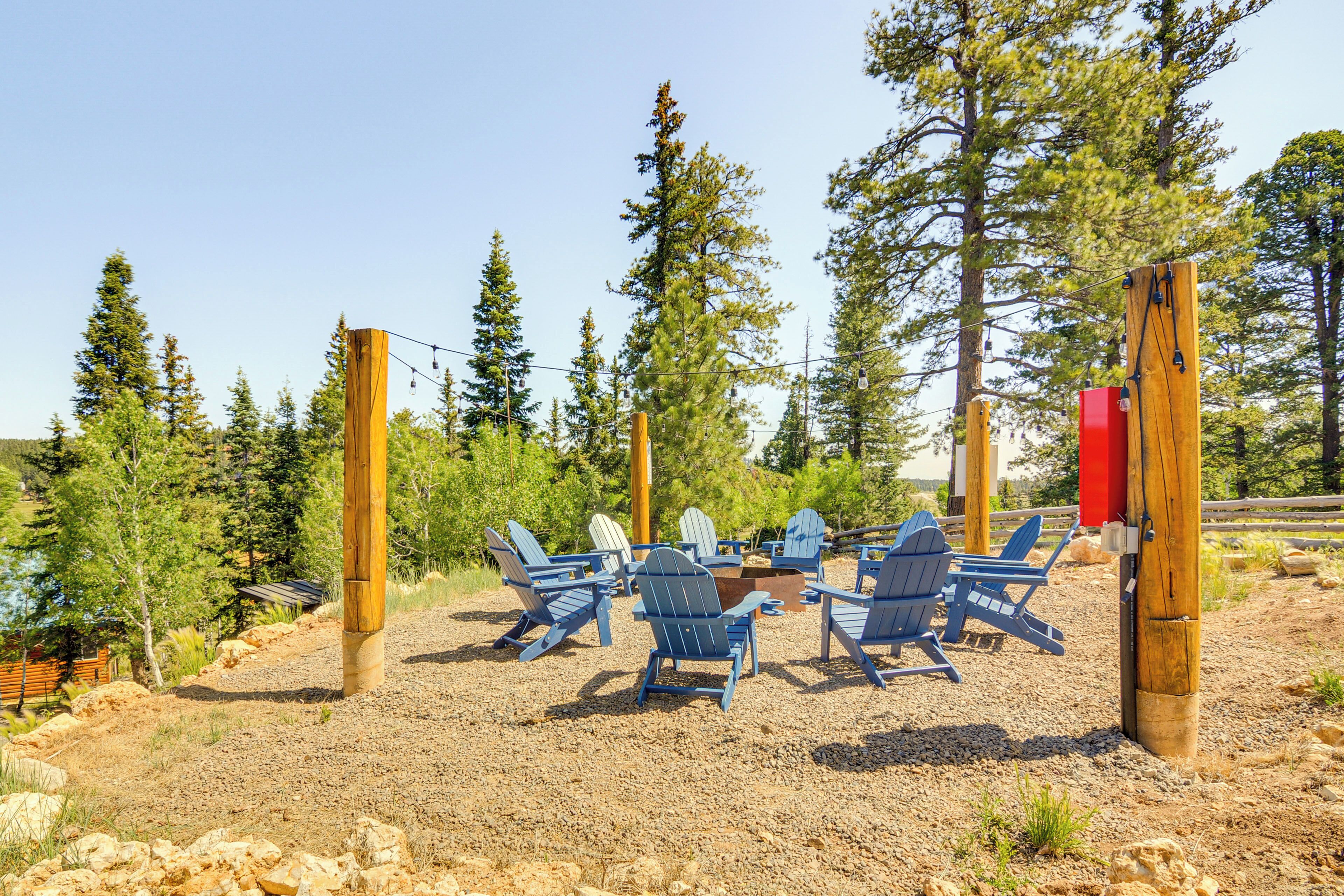 A deck with Adirondack chairs and a fire pit, surrounded by trees.
