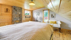 A bedroom with a large bed, wooden ceiling, stone wall, and a window with a view. - Deck & Scenic View: Historic Cabin in Piney Creek! (Piney Creek)