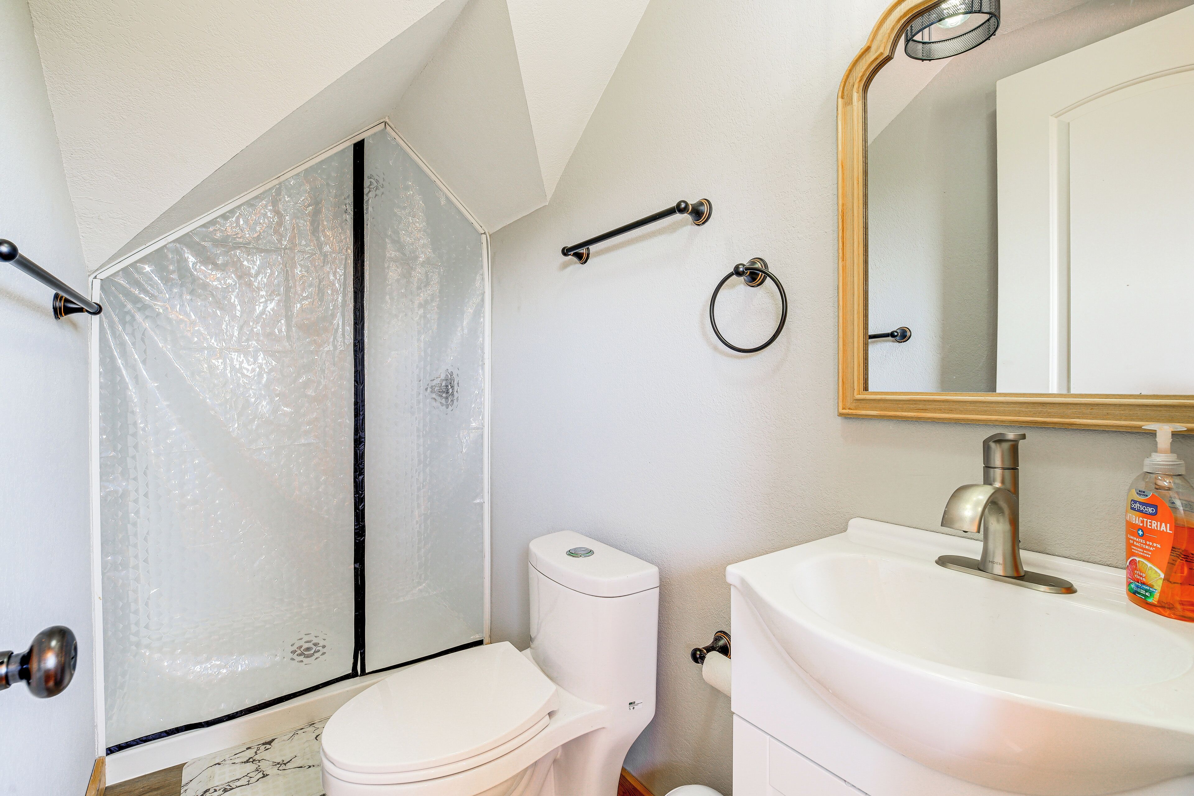A bathroom with a toilet, sink, mirror, and shower enclosure.
