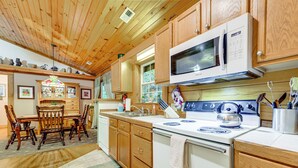 A kitchen with wooden cabinets, a microwave, stove, and a dining area with chairs and a table. - Serene Maggie Valley Retreat w/ Deck & Hot Tub! (Maggie Valley)