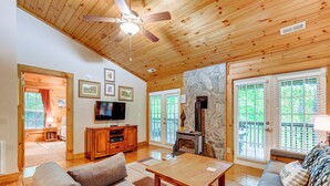 A spacious living room with a wooden ceiling, a stone fireplace, a television, and a stone wall. - Serene Maggie Valley Retreat w/ Deck & Hot Tub! (Maggie Valley)