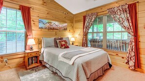 A log cabin bedroom with a bed, nightstands, a window with blinds, and a painting on the wall. - Serene Maggie Valley Retreat w/ Deck & Hot Tub! (Maggie Valley)