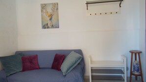 Ein Zimmer mit einem grauen Sofa, einer weißen Bank, einer dekorativen Vase und einem Wandregal.