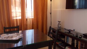 Ein Essbereich mit Tisch, Stühlen, einer Vase, einer Lampe und einem Bücherregal mit Büchern und einem an der Wand befestigten Fernseher.