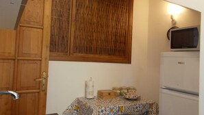 Eine kleine Küche mit Holzausstattung, einer Mikrowelle, einem Kühlschrank und einem Tisch mit gemustertem Tischläufer.