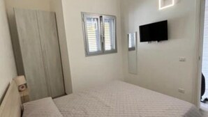 Un dormitorio con cama, armario, ventana y televisor montado en la pared.