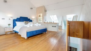 A modern bedroom with a large bed, a wooden floor, a skylight, and a built-in desk area. - Architecturally designed fishing warehouse conversion (Newlyn)