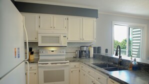 Eine Küche mit weißen Schränken, einer Mikrowelle, einem Backofen, einem Spülbecken und einem Fenster mit Jalousien.