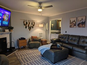 A living room with a television, leather sofa, ottoman, and a patterned rug. - Slopes View! Large Deck/Heated Pool/Hot Tub/Fitness/Sauna/Steam! 2BD/2BA+SofaBed (Beech Mountain)