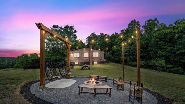 A backyard with a fire pit, wooden tables, and benches, surrounded by a gravel circle. - Rolling Hills/Hot Tub/Firepit/Mins to ACE+NRG (Oak Hill)