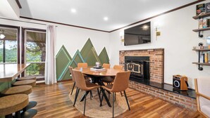A modern dining area with a wooden table and chairs, a fireplace, and a TV mounted on the wall. - Rolling Hills/Hot Tub/Firepit/Mins to ACE+NRG (Oak Hill)